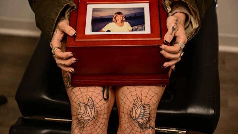 Scout Frank sostiene una caja con las cenizas de su madre previo a ser tatuada por la artista Kat Dukes, el 6 de octubre de 2023 en Oceanside. Foto: AFP
